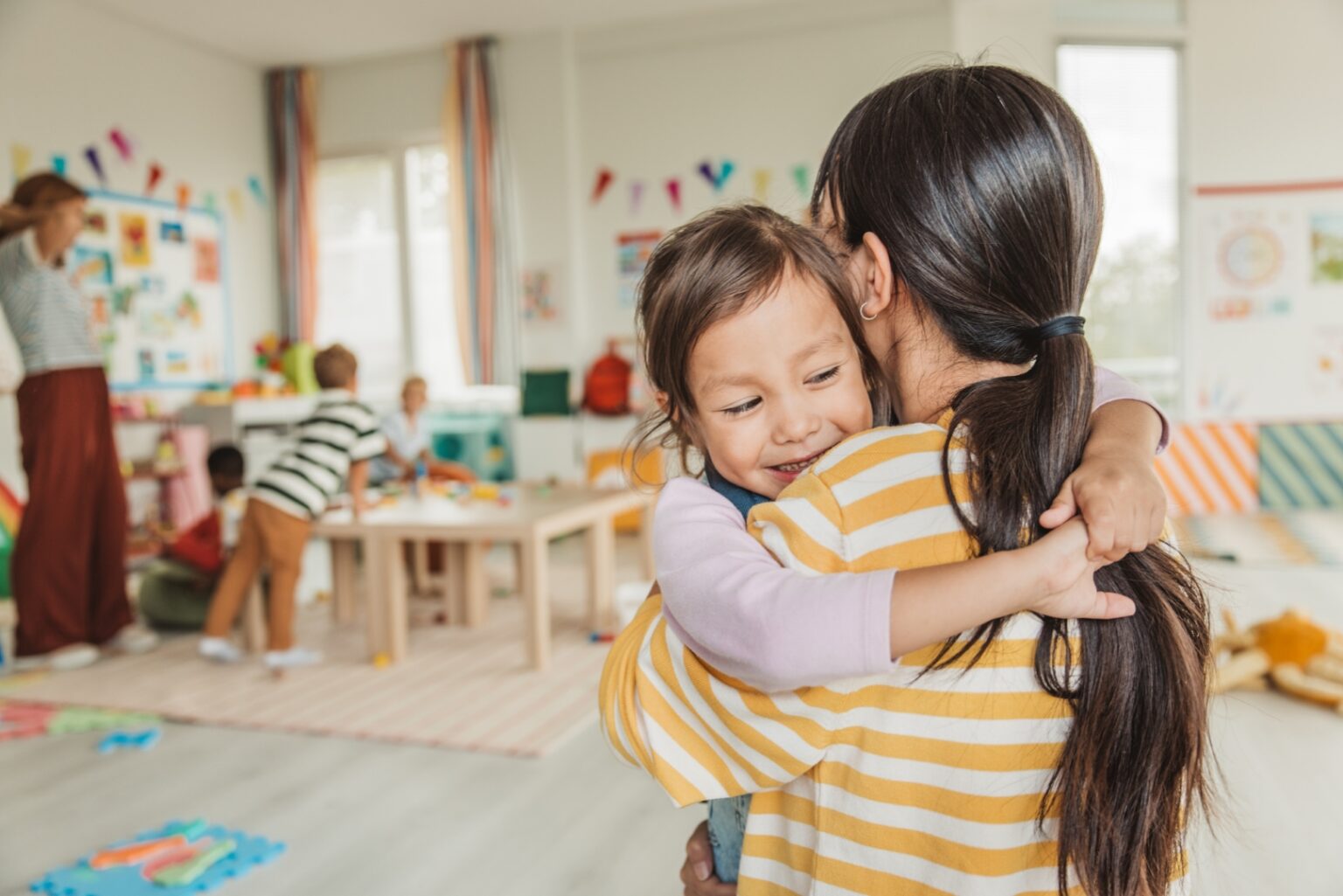 Erzieherin begrüßt ein neues Kind im Kindergarten und unterstützt die Eingewöhnung