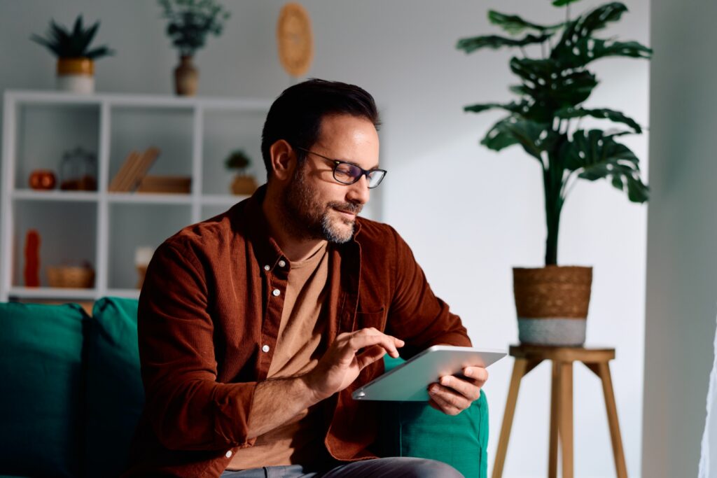 Mann entspannt auf dem Sofa und nutzt ein digitales Tablet zu Hause